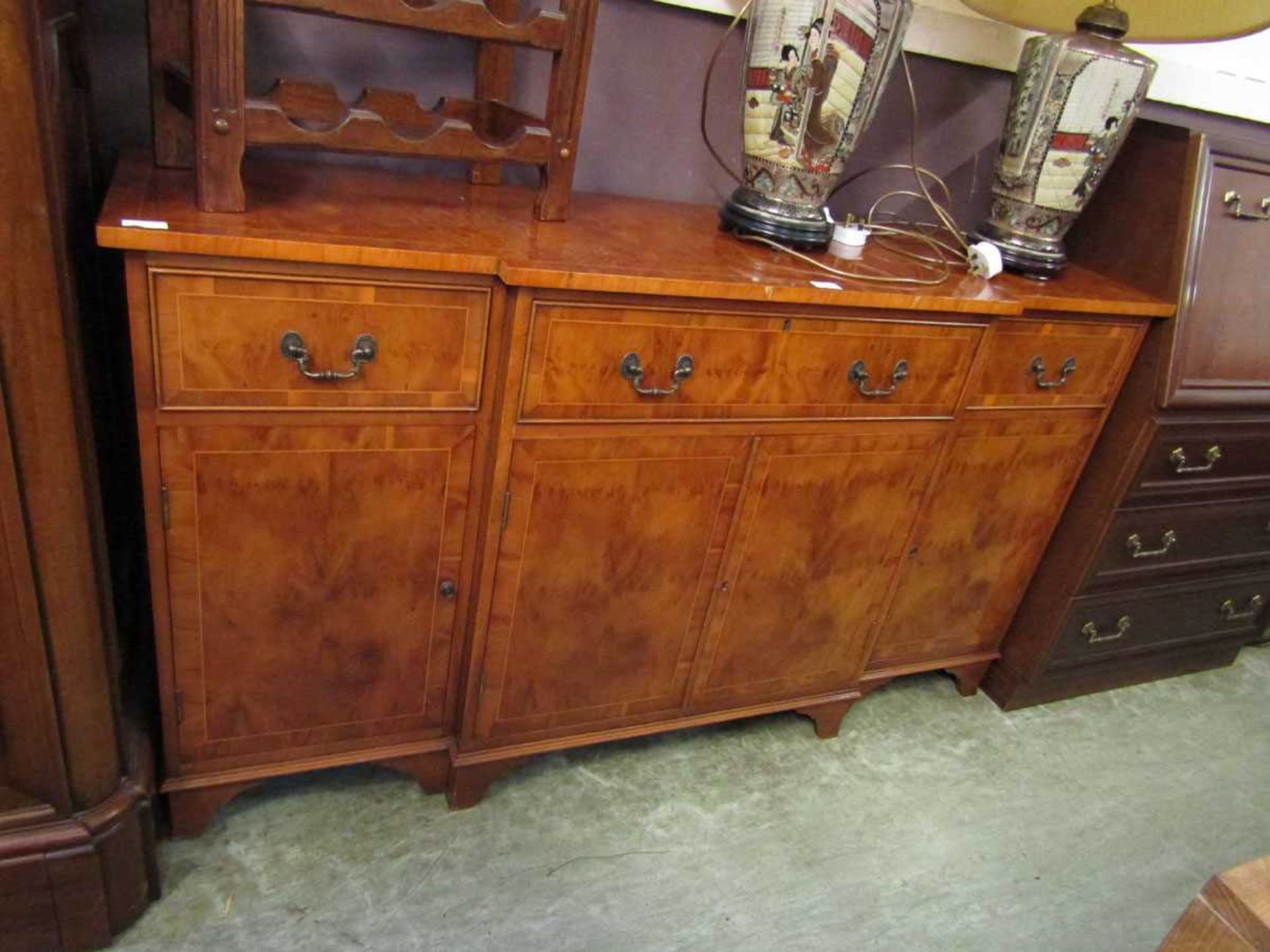 A reproduction break front yew sideboard having a centre drawer above cupboard doors flanked by