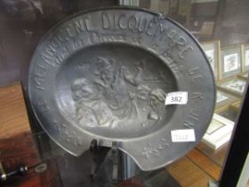 A pewter barbers bleeding bowl depicting classical figures with embossed text 'Le Milanogene