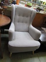 A modern high back wing armchair upholstered in a light grey fabric