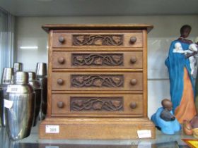 An oak desktop chest of four drawers with carved floral panel to front of drawers