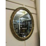 An ornate gilt framed oval bevel glass wall mirror