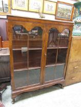 An early 20th century walnut veneered glazed two door display cabinet on cabriole supports