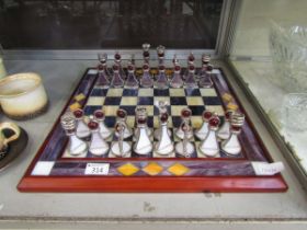 A wood and coloured glass chess board along with a set of white and purple glass chess pieces