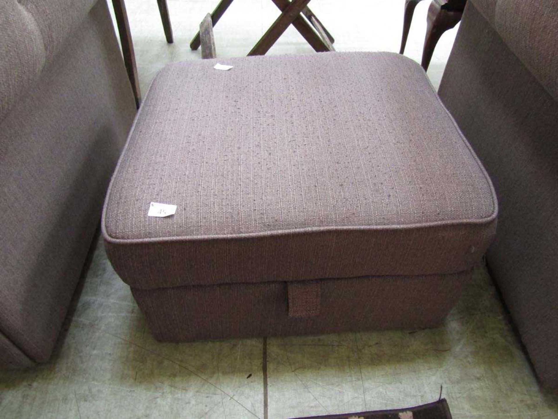 A brown upholstered modern pouffe with lift up lid concealing storage space