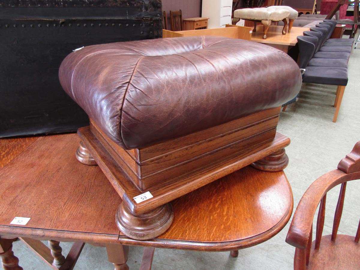 A reproduction oak foot stool having a brown leather upholstered cushion to top
