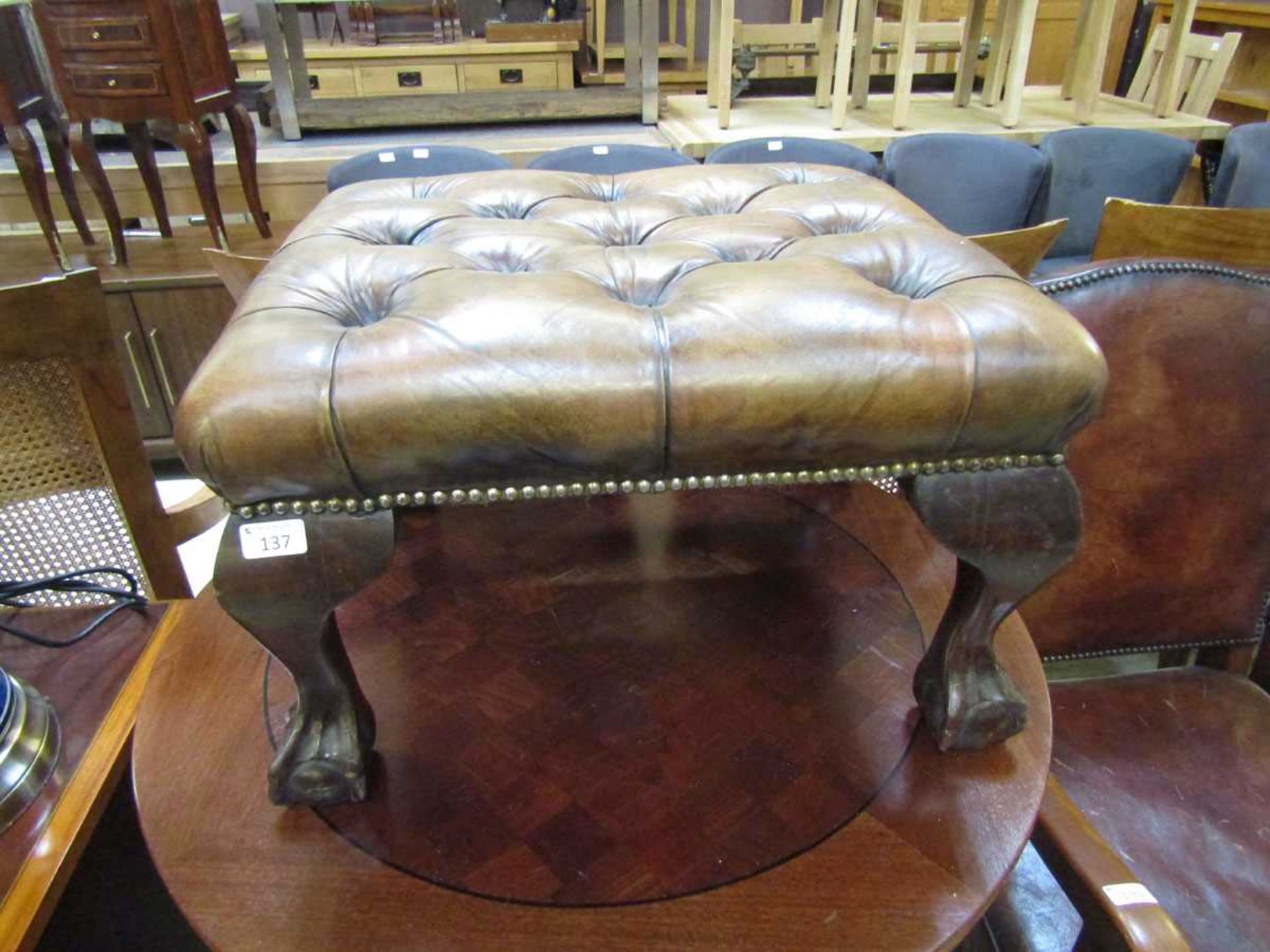 A reproduction mahogany footstool having a button leather upholstered seat on ball and claw feet