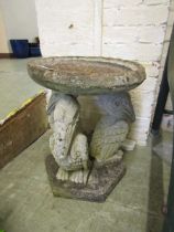 A weathered stoneware garden birdbath having a pelican design