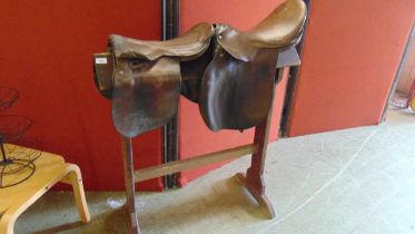 An early 20th century wooden saddle horse together with two distressed leather saddles