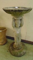 A weathered stoneware bird bath with cherub column