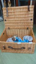 A wicker picnic basket with a collection of blue and white striped plates, mugs, bowls, etc