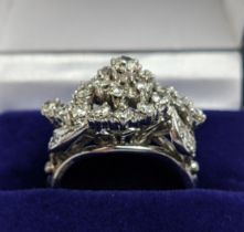 A WHITE METAL AND DIAMOND CLUSTER RING, the centre with a flower head setting surrounded by C