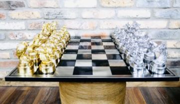 CHESS SET, chequered board complete with silvered and gilt finish animal form pieces, 60cm x 60cm.