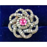 A RUBY AND DIAMOND DRESS RING, white metal shank, the flower head setting with a central ruby