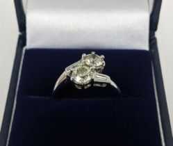 AN 18CT WHITE GOLD TWO STONE DIAMOND CROSS-OVER RING, each round brilliant cut stone of