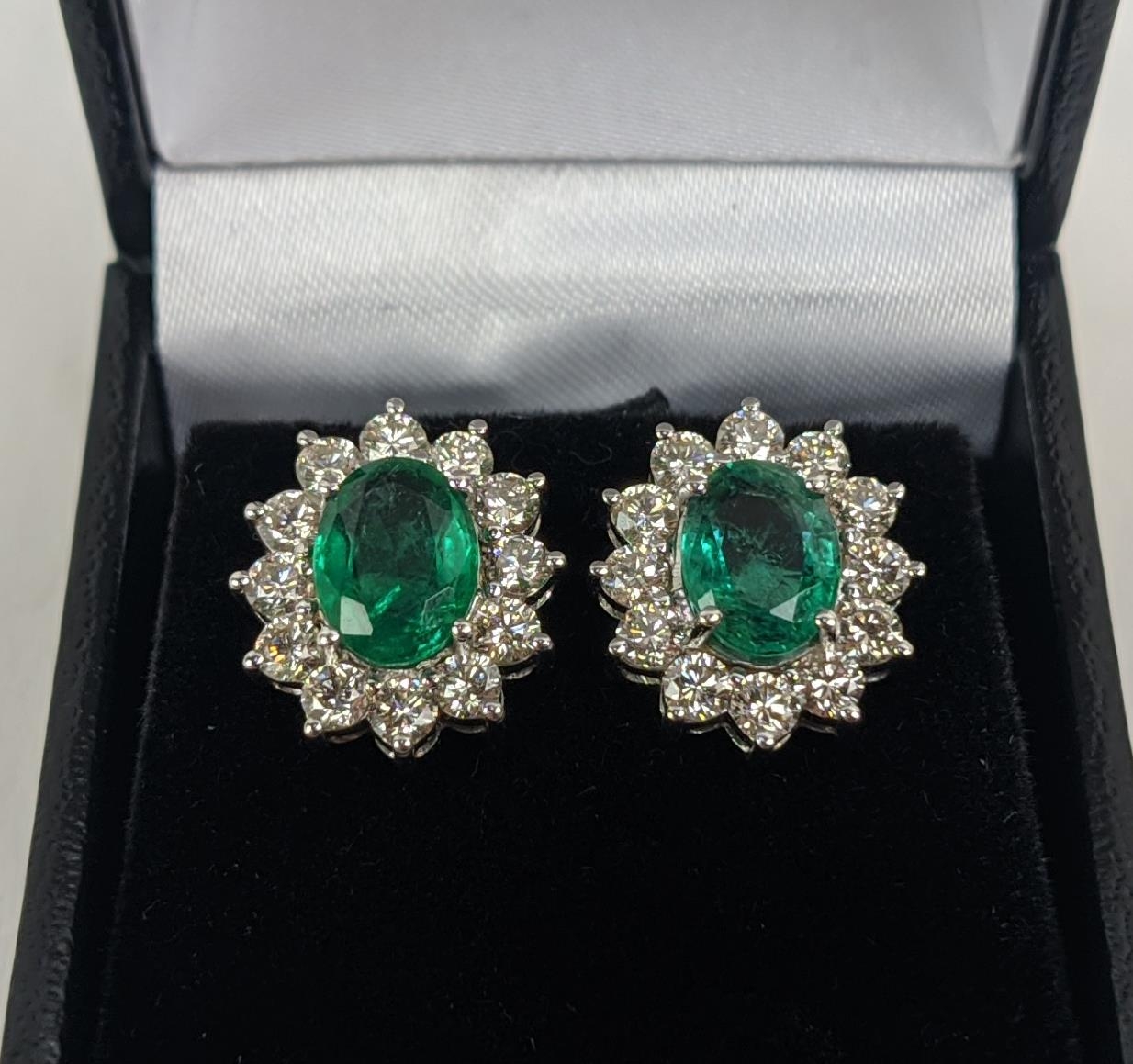 A PAIR OF 18CT WHITE GOLD EMERALD AND DIAMOND CLUSTER STUD EARRINGS, the oval mixed cut emerald