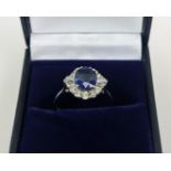 AN 18CT WHITE GOLD SAPPHIRE AND DIAMOND HALO RING, the central oval mixed cut sapphire of