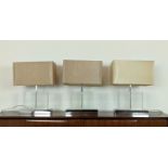 TABLE LAMPS, a set of three, glass on polished metal bases, each 52cm H overall including shades. (