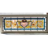 STAINED GLASS PANEL, mask and foliate scroll design in painted frame, 35cm H x 91cm.