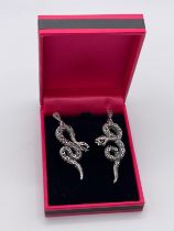 A pair of silver earrings in the form of coiled serpents, each snake with textured body and inset