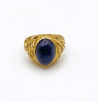 A yellow gold and lapis lazuli ring, set with an oval polished stone, within an ornate textured