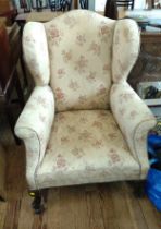 An antique wing-back arm chair, upholstered in cream floral fabric, on shaped wooden legs.