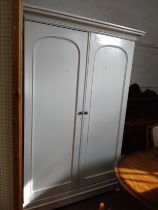 A large two-door wardrobe, painted white and with a hanging rail. The wardrobe sits on a plinth on