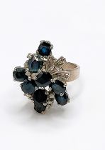 An 18k white gold, diamond, and sapphire asymmetric cluster ring, set with nine mixed round and