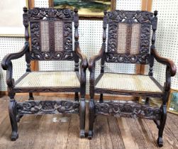 A pair of carved oak framed arm chairs, with cherub and scroll decoration, with wicker seats, carved