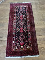 A red and black ground rug with symmetric pattern detail, fringed. 208cm x 91cm