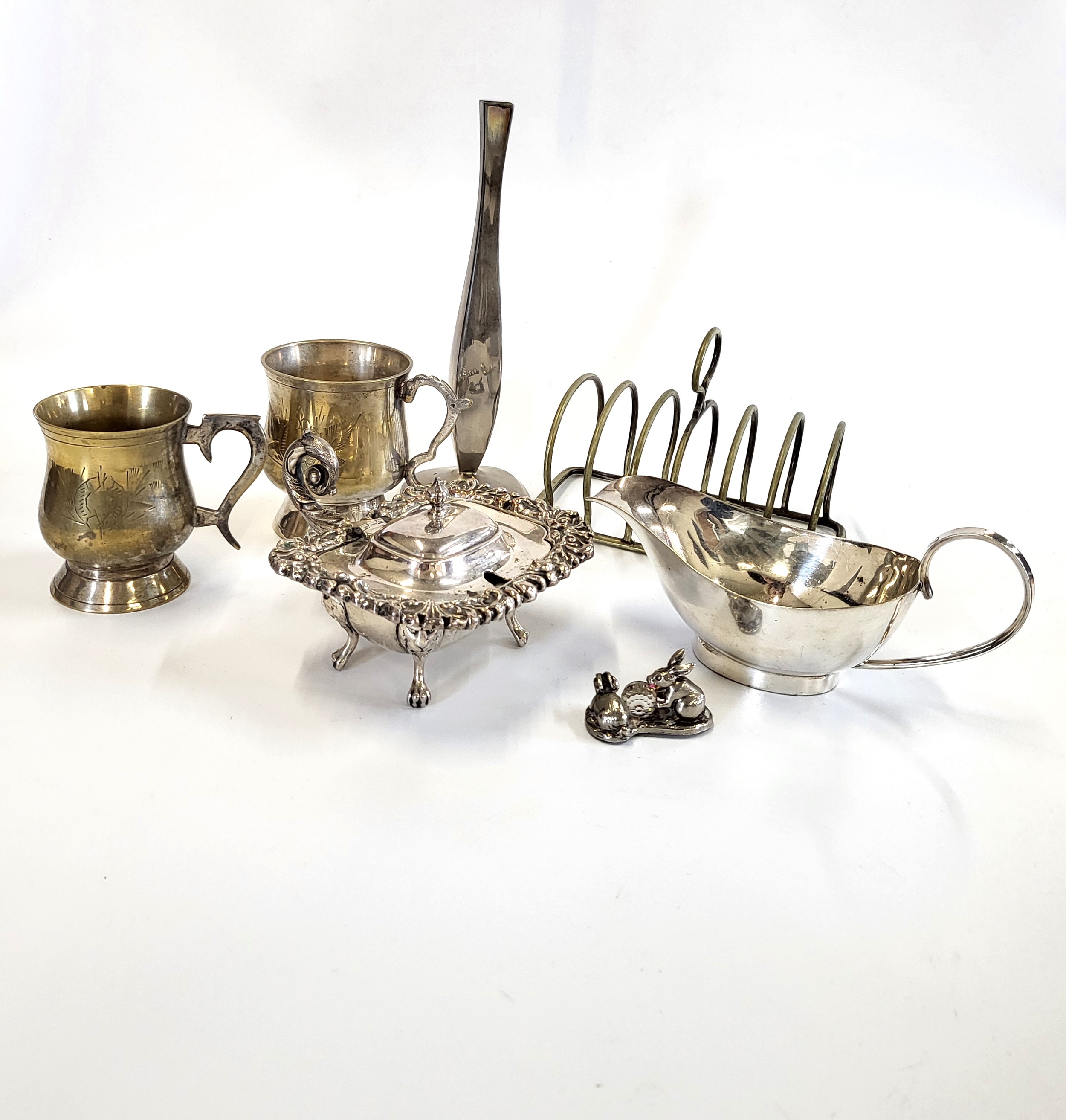 A group of silver plated items, including two mugs, a toast rack, a posy stem vase, and a white