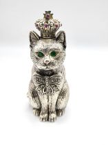 A novelty pin cushion in the form of a seated cat with green eyes, wearing a crown, with red