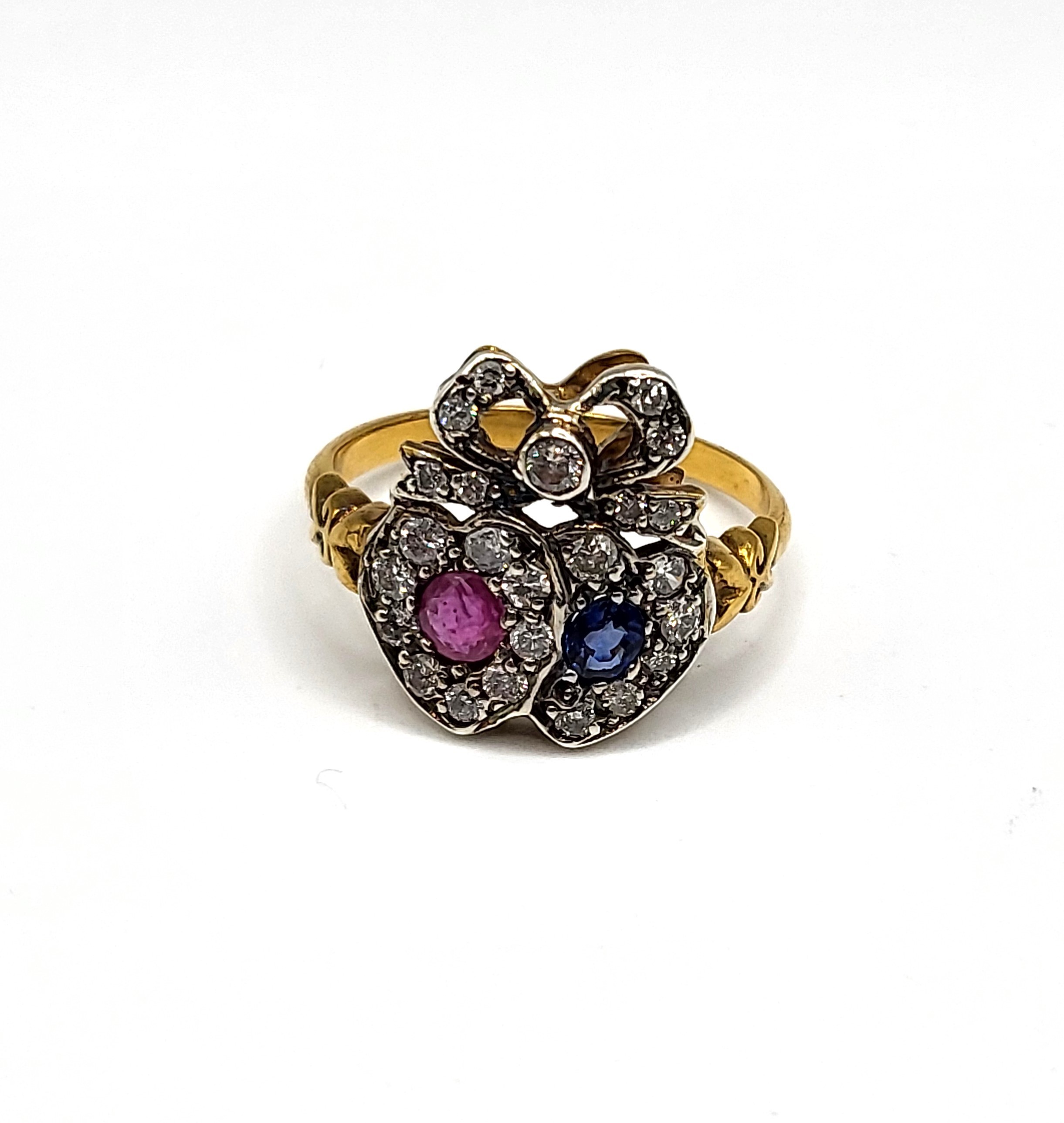A diamond, ruby, and sapphire sweetheart ring, the ribbon-twist mount inset with round-cut diamonds,