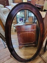 An Edwardian oval mirror in dark wood frame. 110cm x 64cm.