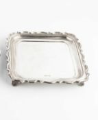 A George V silver square salver, with shaped border, on foliate scroll feet by Walker & Hall,