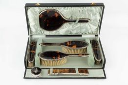 A silver mounted tortoiseshell backed dressing table set, comprising hand mirror, two hair