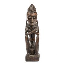 An antique carved wood tribal seated figure possibly Malaysian. 8cm wide 32cm high.