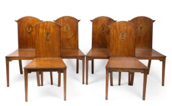 A set of six George III and later mahogany hall chairs with armorial crests on the back panel with
