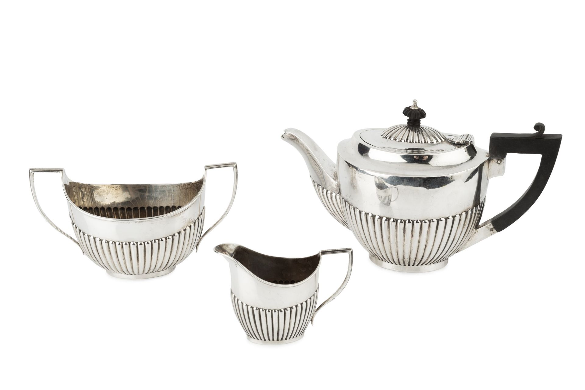 A matched silver three piece tea service, of half lobed form, the teapot with ebonised handle and