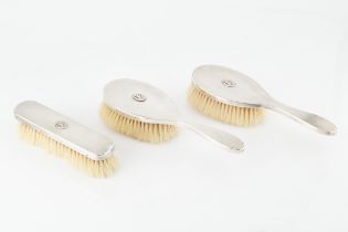 A silver three piece dressing table set, comprising two hair brushes and a clothes brush, with