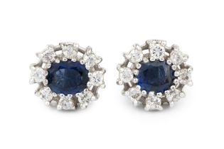 A pair of sapphire and diamond cluster ear studs, each set with an oval cut sapphire within a border
