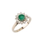 An emerald and diamond cluster ring, the central circular emerald within a border of twelve