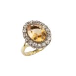 A topaz and diamond cluster ring, the oval central orange-brown topaz within a border of seventeen