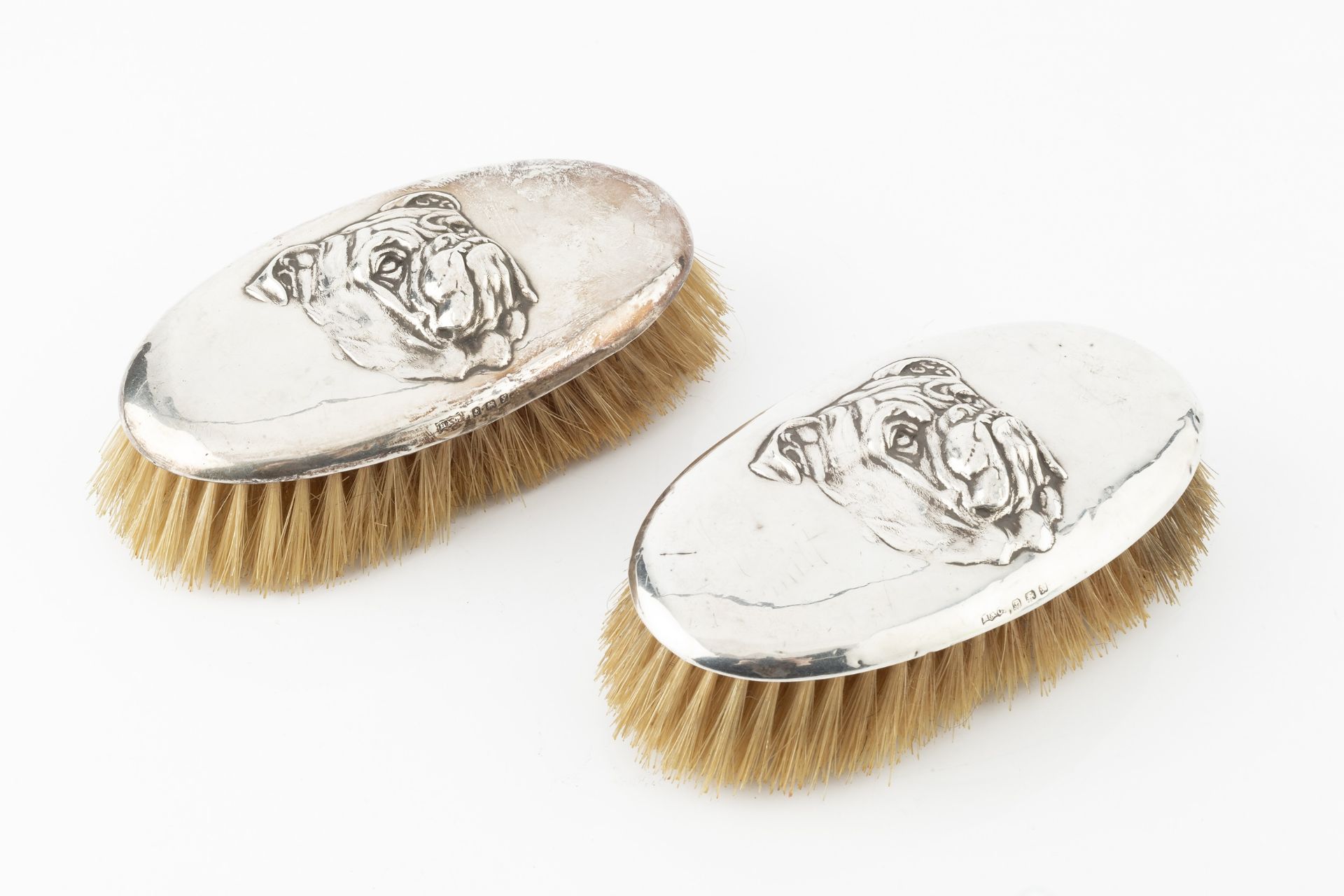A pair of George V silver backed clothes brushes, each relief decorated with the head of a