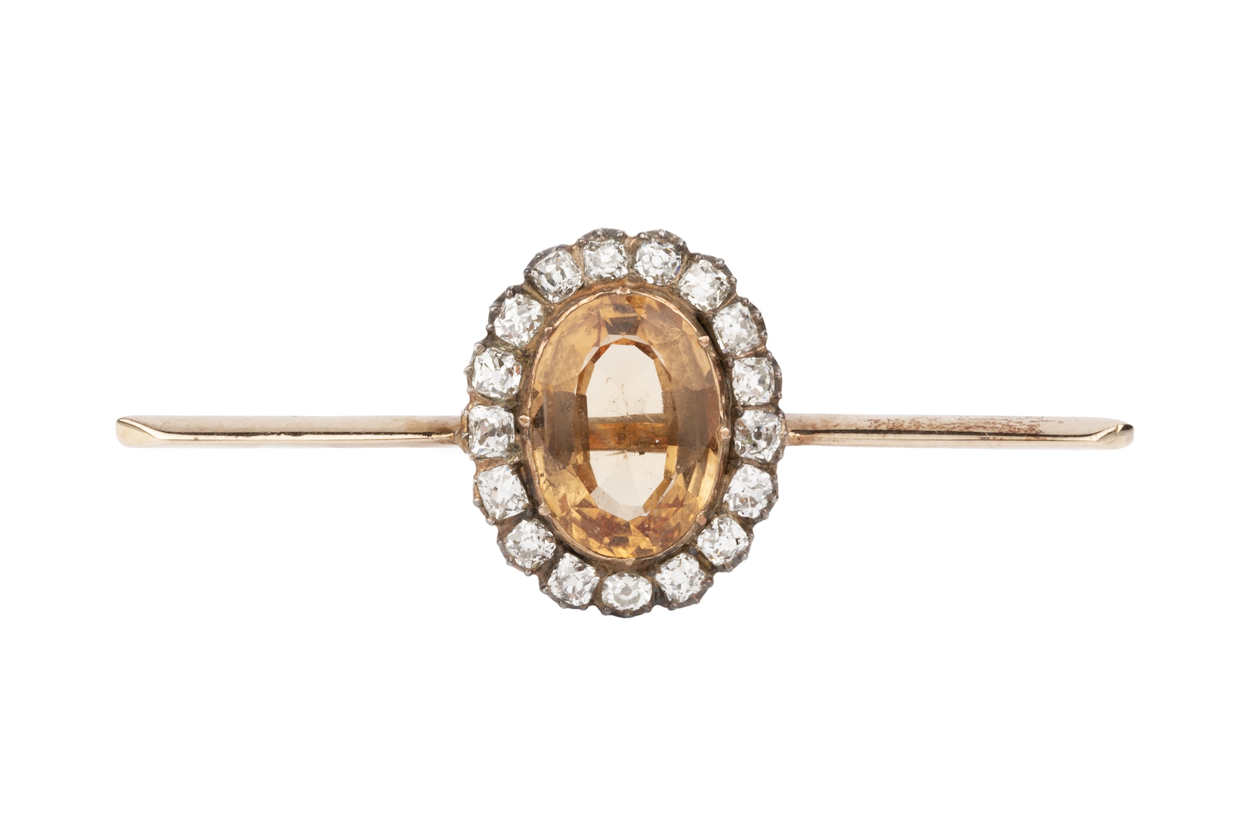A topaz and diamond mounted bar brooch, the oval orange-brown stone within a border of seventeen