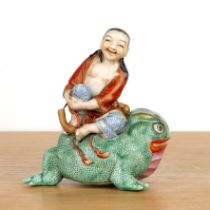 Porcelain model of a boy on a toad Chinese, Republic period holding his hands under his knee,