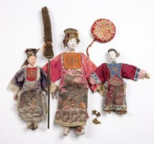 Three wooden dolls Chinese to include a female doll in a fuchsia ground gown, the gown embroidered