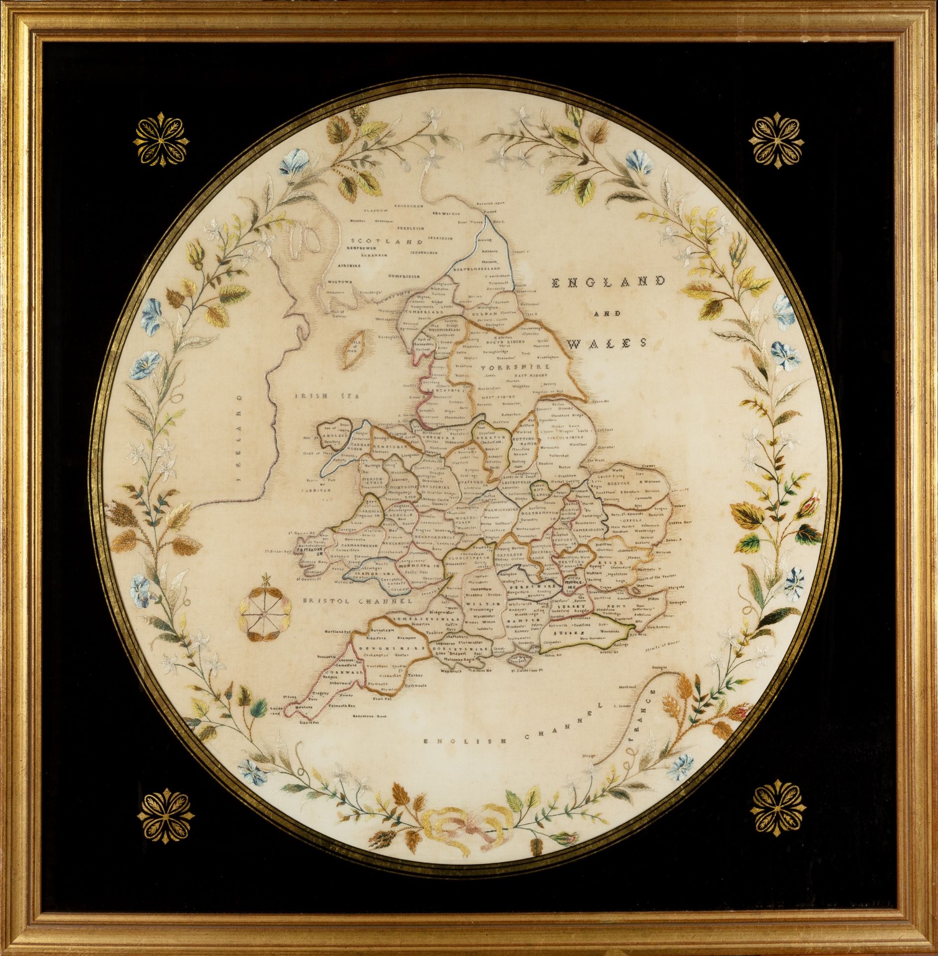 A 19th century embroidered map of England and Wales with a floral border 54cm diameter. mounted in a
