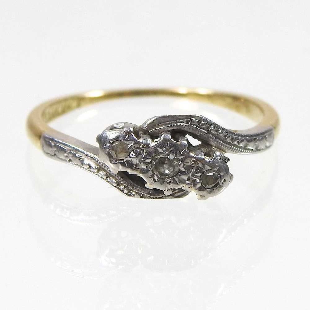 An 18 carat gold and platinum set three stone diamond ring, of crossover design, with textured