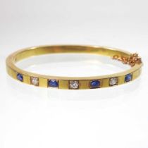 An early 20th century 18 carat gold sapphire and diamond bangle, of hinged design, set with a row of