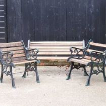 A wooden garden bench, with green painted metal supports, together with a pair of matching armchairs